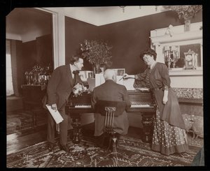 Clara De Regand wijst naar een partituur terwijl een man piano speelt, 1910